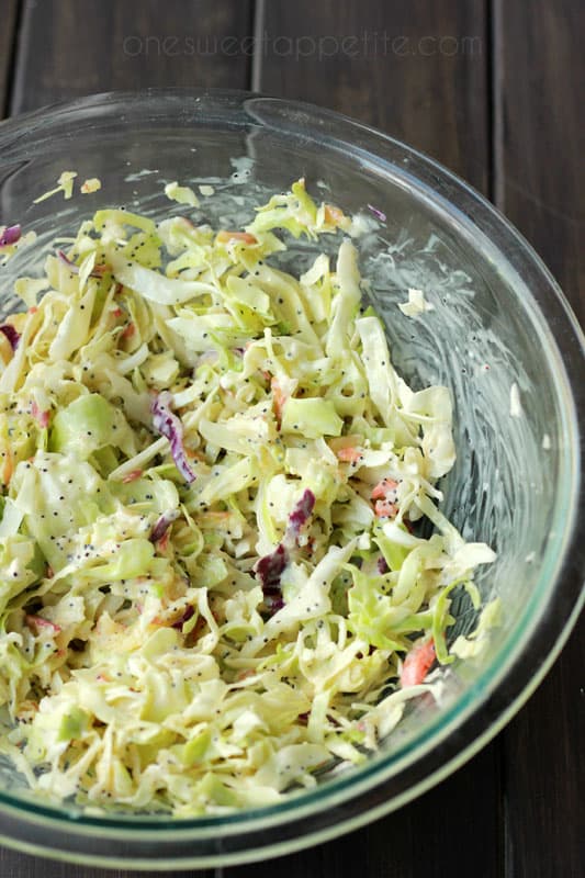 coleslaw in a glass mixing bowl sitting on a dark brown wooden table