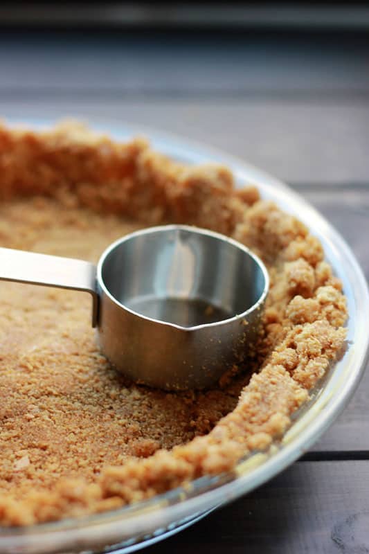 measuring cup packing down a pie crust inside a glass pie dish