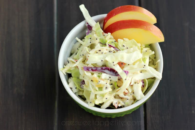 small green bowl filled with a coleslaw with two apple slices on top on a dark brown wood table