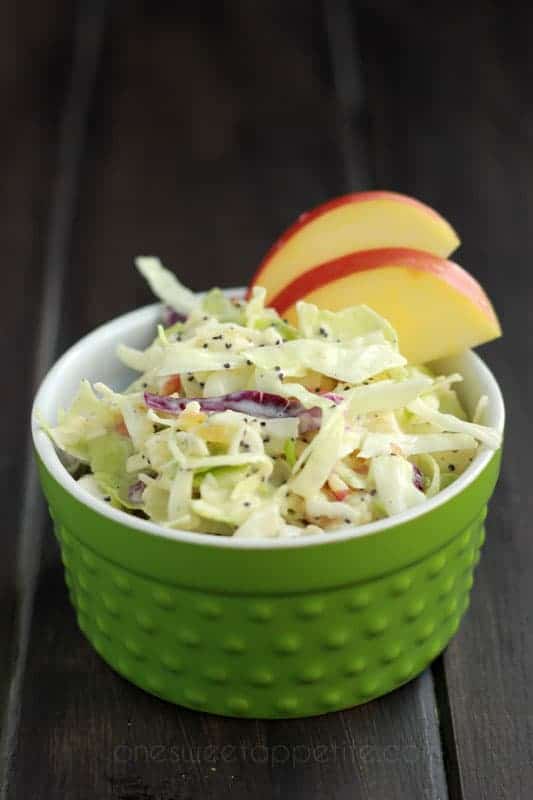 small green bowl filled with a coleslaw with two apple slices on top on a dark brown wood table