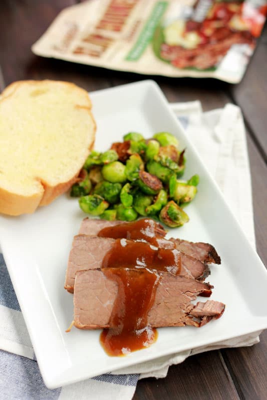 close up image of a pot roast slice on a rectangle plate with roasted brussels sprouts and a garlic toast