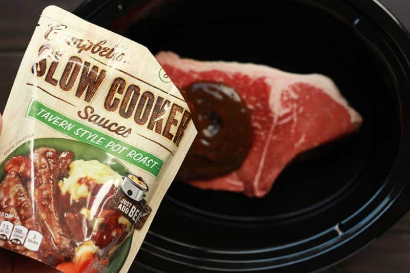 Campbell's sauce being poured on top of a chuck roast inside of a slow cooker