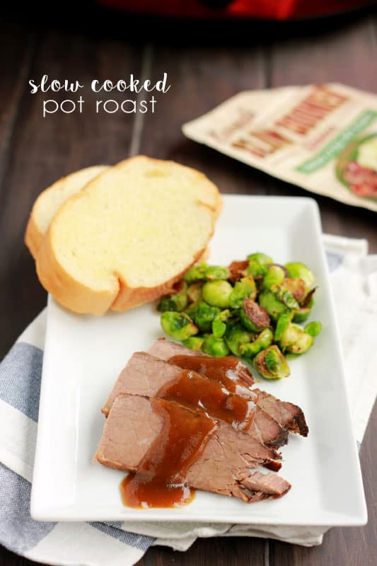 white rectangle plate with slices of pot roast drizzled with gravy, cooked brussels sprouts, and garlic toast