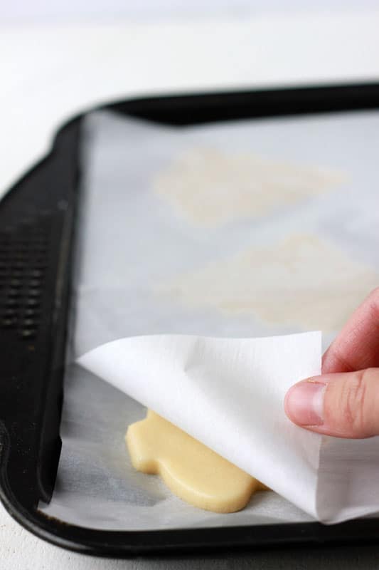 cut out shaped sugar cookies on a parchment lined tray with parchment on top