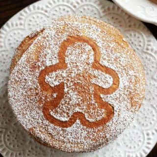 stack of gingerbread pancakes on a white plate with a dusting of powdered sugar in the shape of a gingerbread cookie