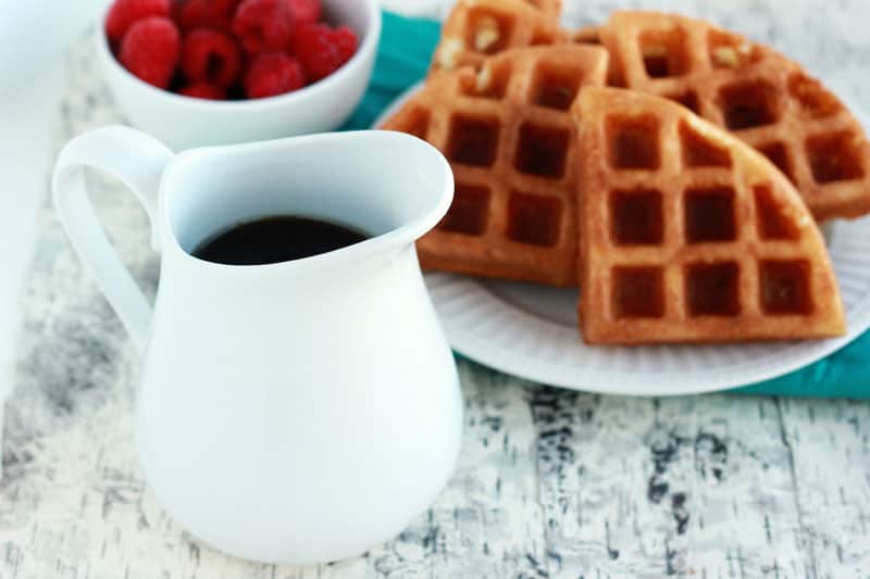 White pour dish filled with syrup sitting next to a plate of waffles