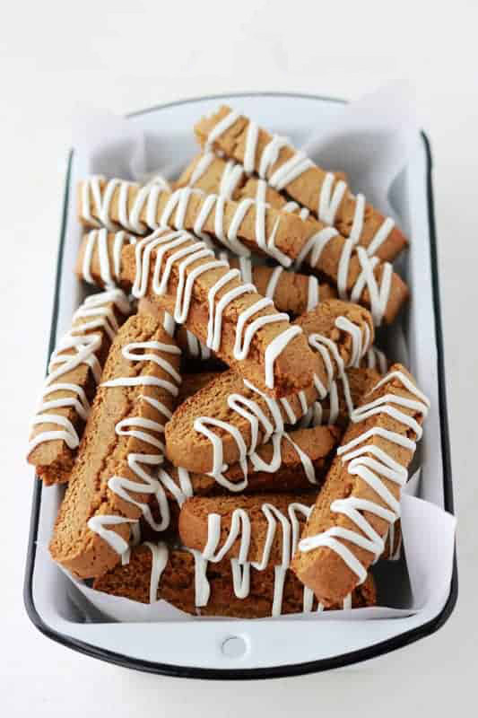 tin full of gingerbread biscotti that is topped with white frosting