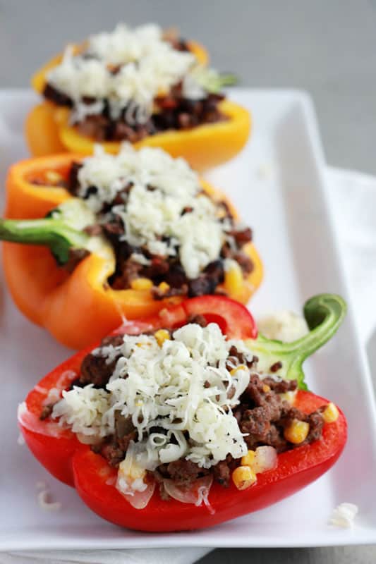 Stuffed peppers lined on a white plate topped with shredded cheese