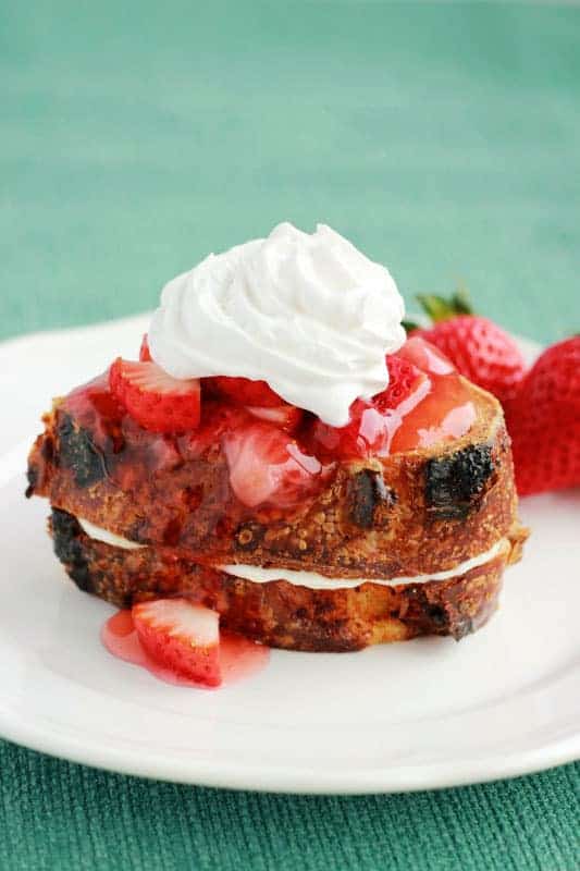 stuffed french toast on a white plate topped with strawberry sauce and whipped cream
