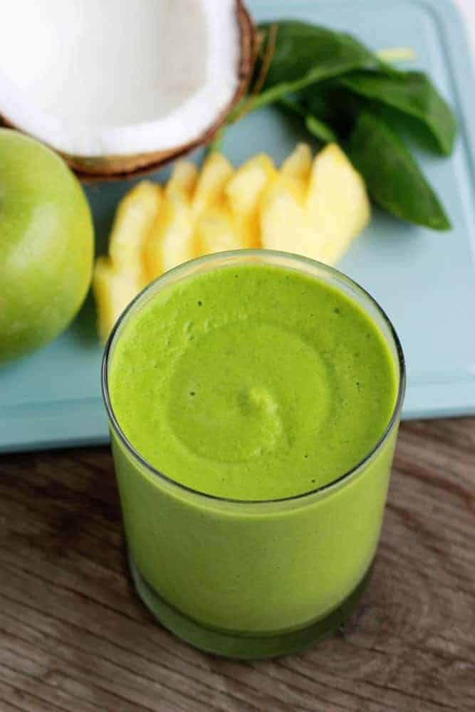 close up image of a green smoothie with pineapple slices and fresh coconut
