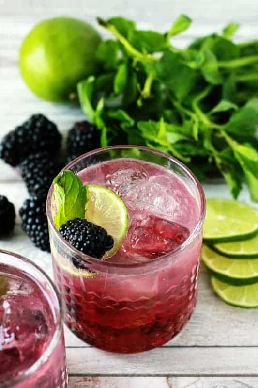 glass filled with a blackberry mojito topped with fresh lime, berries, and mint