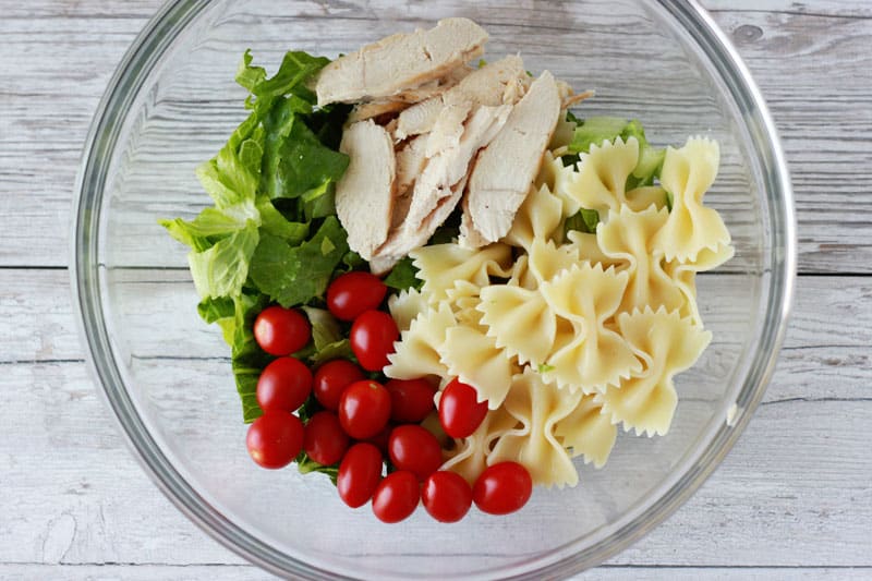 Pasta salad ingredients in a glass bowl ready to be mixed