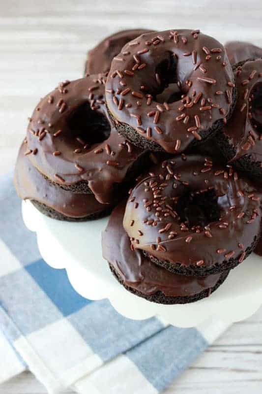 Chocolate donuts stacked on a white cake stand.