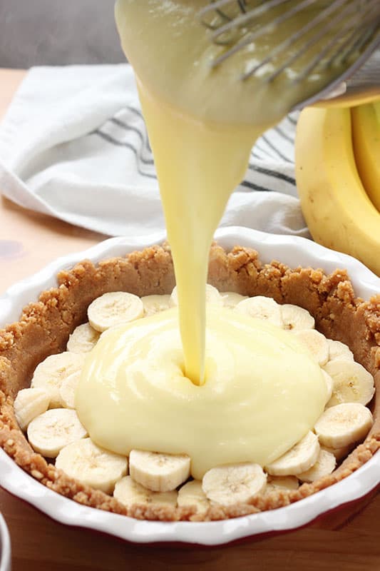 warm pudding pouring over top of a pie crust filled with bananas