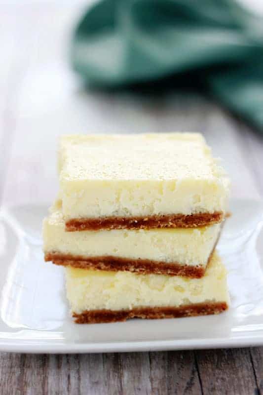 close up of three cheesecake bars stacked on a small white plate