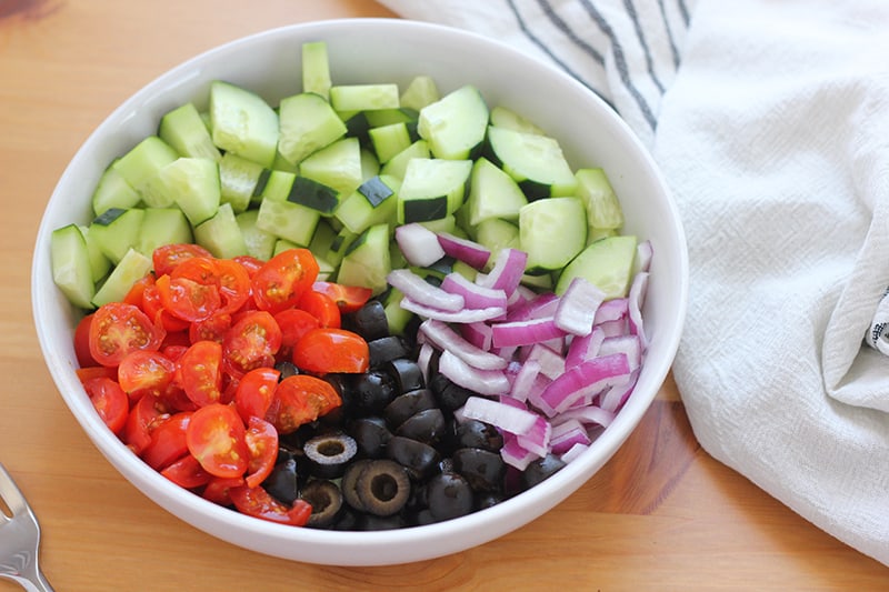 large white shallow bowl filled with cucumber, tomato, red onion, and olives