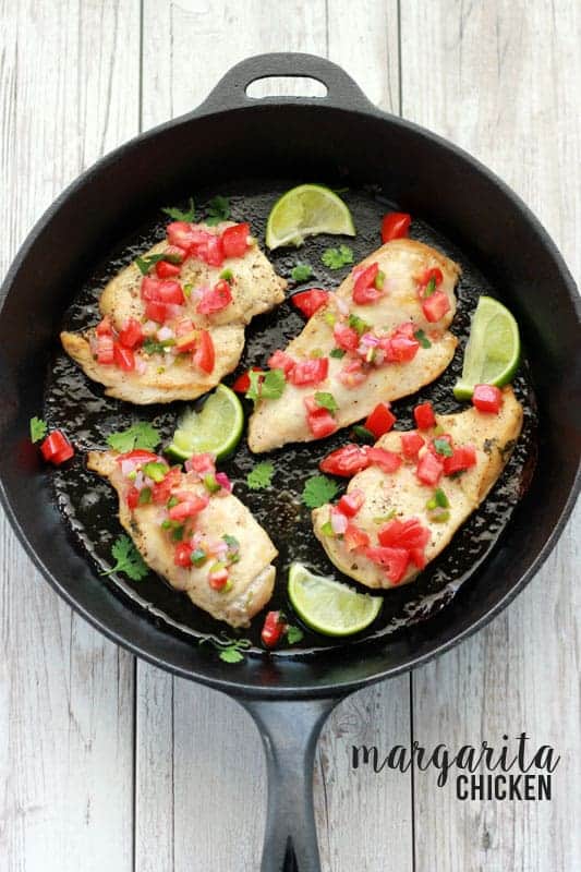 chicken sitting inside of a cast iron pan topped with fresh pico and lime wedges