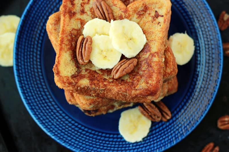 close up image of a stack of french toast topped with bananas and pecans