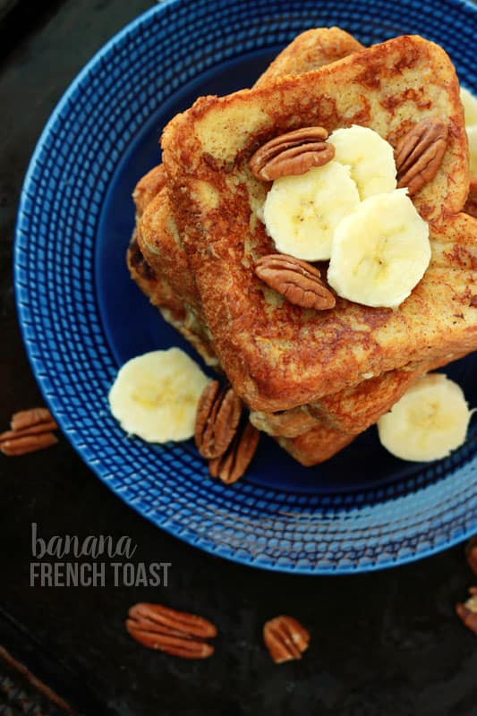 stack of french toast topped with fresh banana slices and pecans on a dark blue plate.