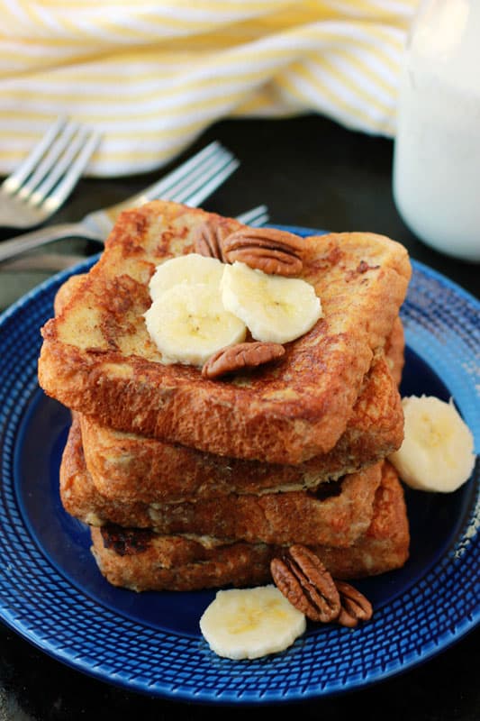 Banana French Toast stacked on a blue plate and topped with fresh banana slices