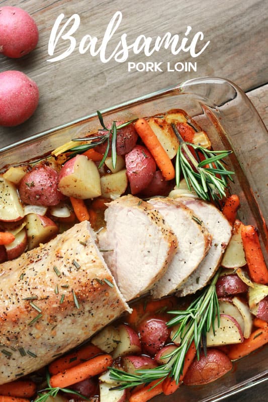 top down image of a baked pork roast sitting on baked vegetables inside a 9x13 dish on a light brown wooden tabletop 