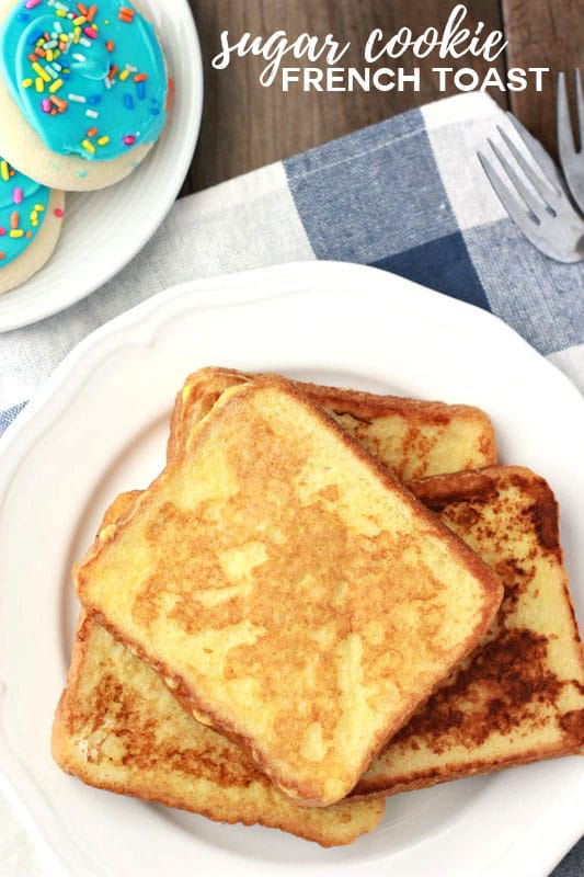 cooked french toast stacked on a white plate with blue frosted sugar cookies set to the side