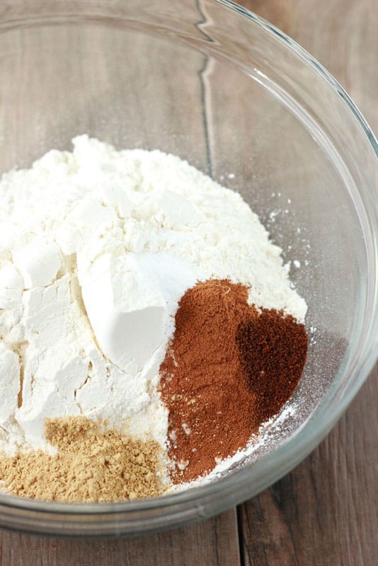 flour and spices in a glass bowl on a wooden countertop.