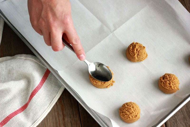 cookie dough rounds on a baking tray being pressed down by a spoon