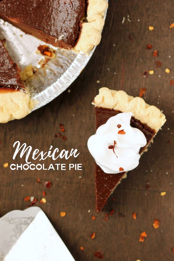 top down image showing a slice of chocolate pie with a dollop of whipped cream and  a sprinkle of red pepper flakes on a dark wooden table