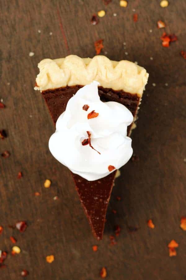 Top down image of a slice of chocolate pie that is topped with whipped cream with a sprinkle of red pepper flakes