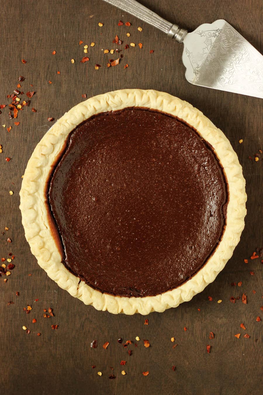 whole chocolate pie sitting on a wooden board with sprinkles of red chili flakes off to the side