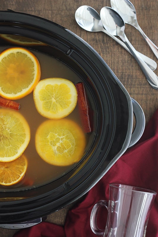top down image of a slow cooker filled with cider that is simmering with orange slices and cinnamon sticks