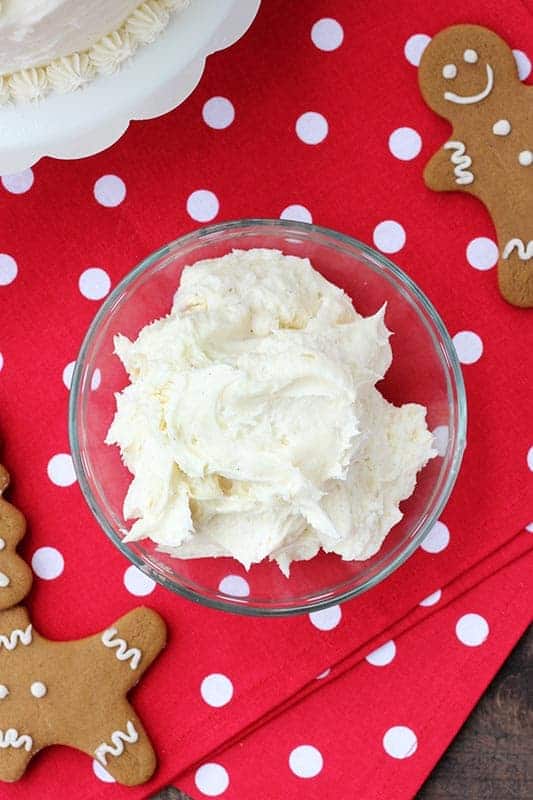 glass bowl filled with frosting on a red polka dot napkin with gingerbread cookies surrounding 