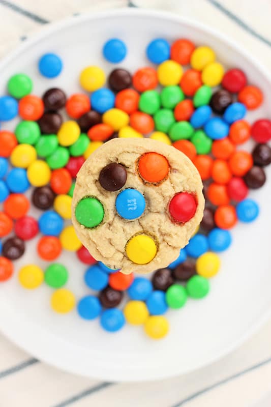 top down image showing a mm cookie hovering over the top of a white plate that is filled with mm candies