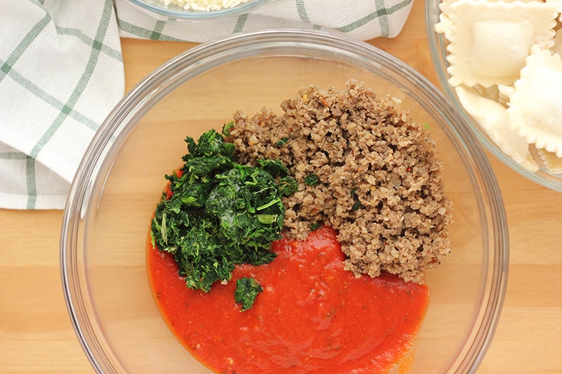 pasta sauce, cooked and crumbled sausage, and spinach in a large bowl- Ravioli Bake Sauce
