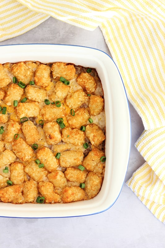 top down image close up of a tater tot hot dish that is sitting on a white table top with a yellow and white stripe napkin off to the side