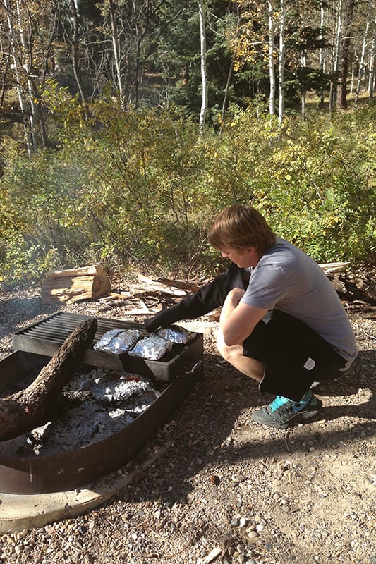 man turning tin foil dinners over a campfire 