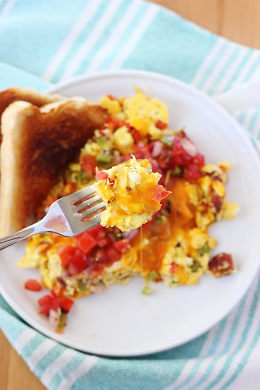 Small round white plate with a lifted edge topped with cheese pico topped scrambled eggs and two slices of toast