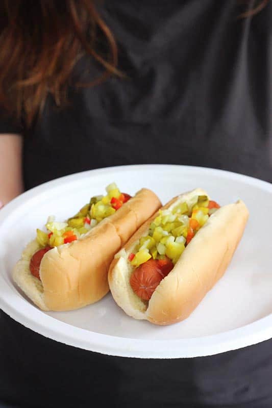 white paper plate with grilled hotdogs topped with relish