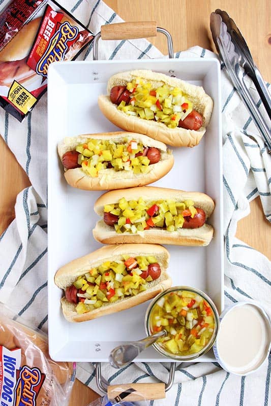 white platter with hot dogs in buns topped with relish