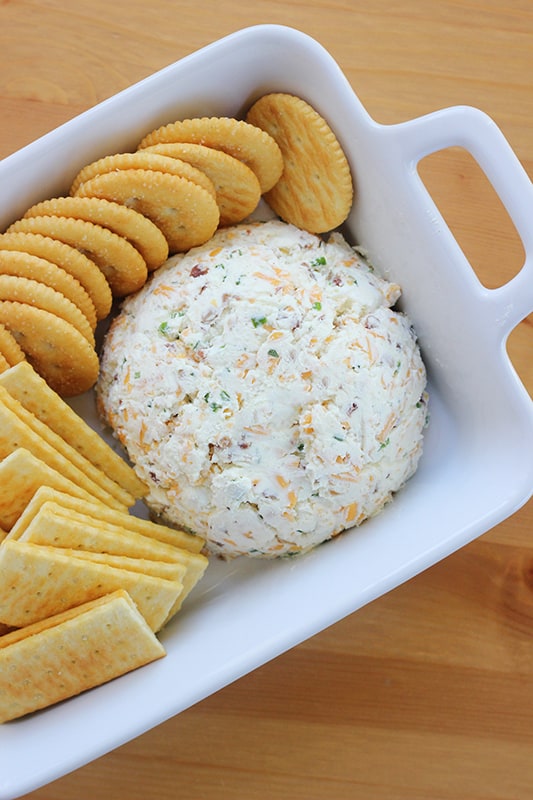 top down image showing a cheese dip in the shape of a ball in a white rectangle serving dish with crackers spread around the dip. 