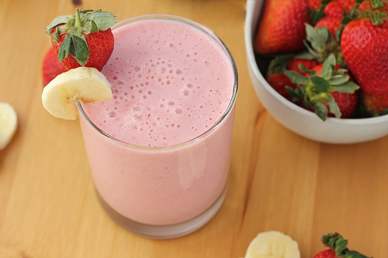 close up image of a strawberry smoothie with a slice of banana and fresh berry