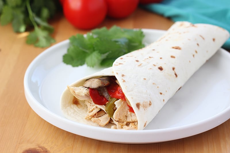 chicken and peppers wrapped in a tortilla served on a white plate