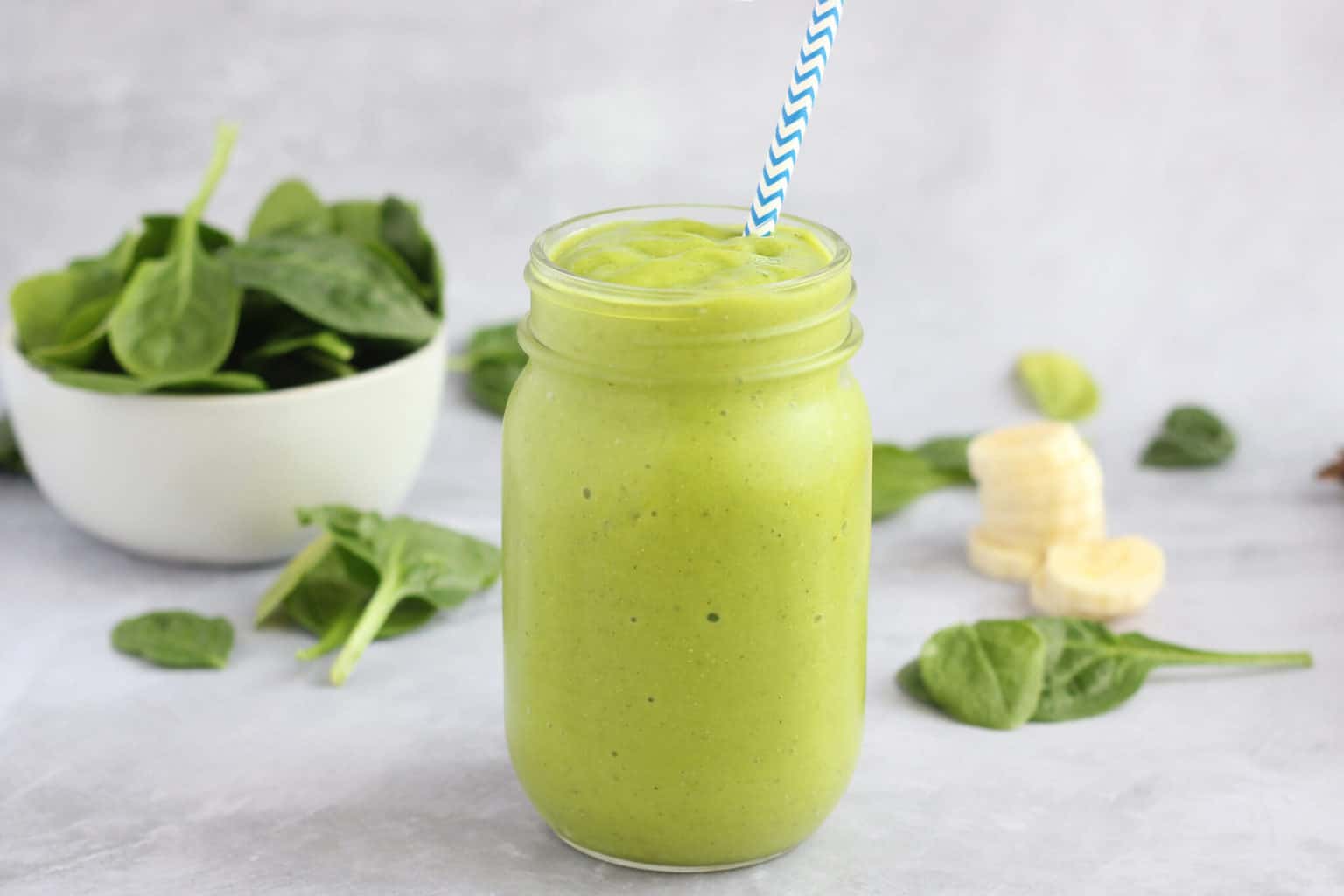 green smoothie in a mason jar with a blue straw