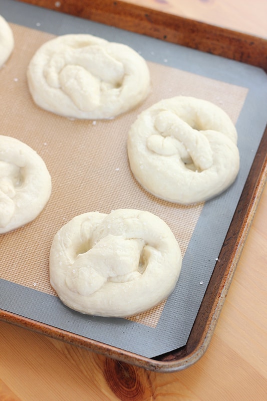 boiled pretzels waiting to be baked on a mat lined baking tray