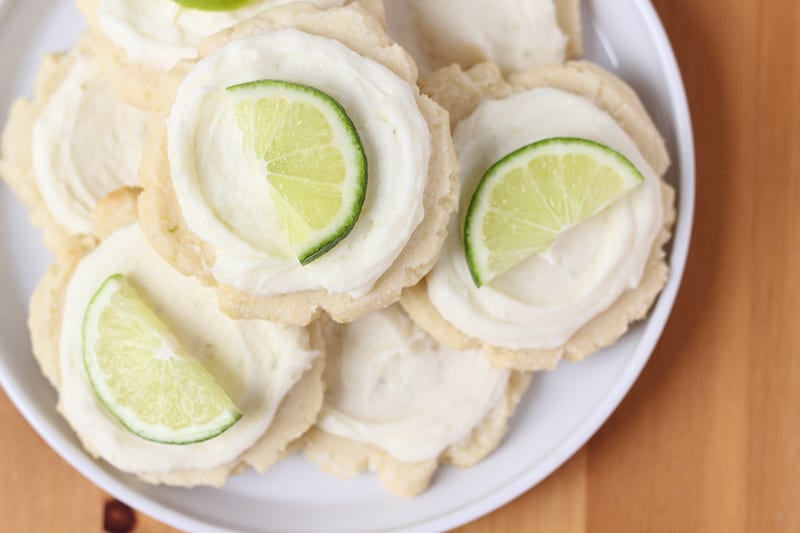 Frosted sugar cookies on a white plate with slice of lime