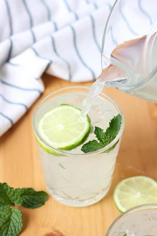 limeade pouring into glass with lime slice and mint leaves