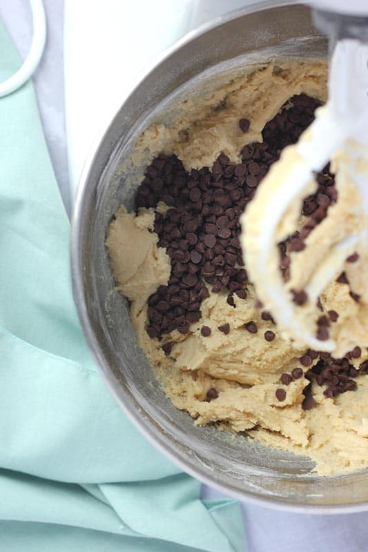 cookie dough inside a metal mixing bowl with mini chocolate chips and a paddle attachment 