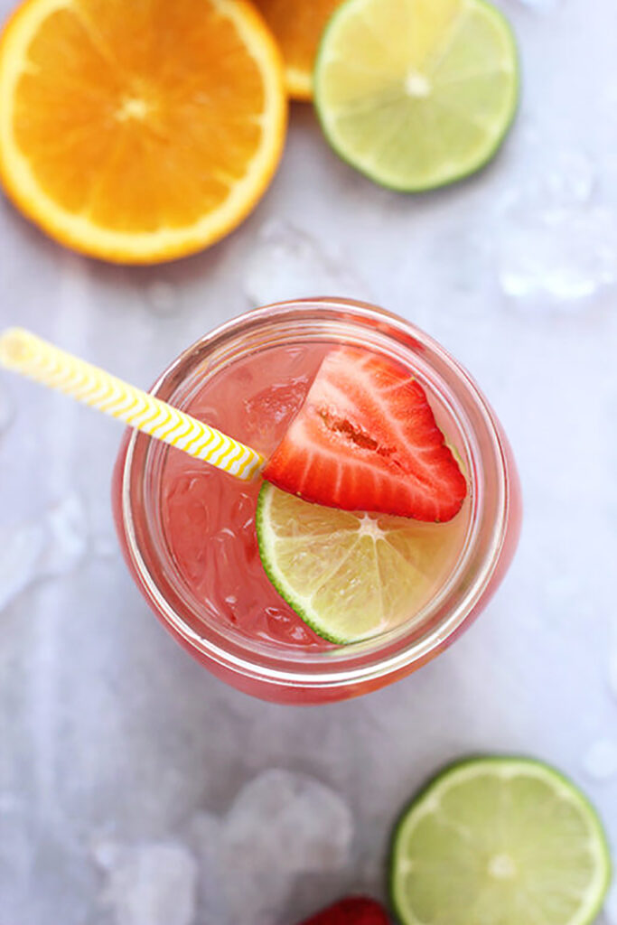 top down image of a glass filled with pink punch and topped with a fresh lime slice and strawberry slice sitting on a grey background