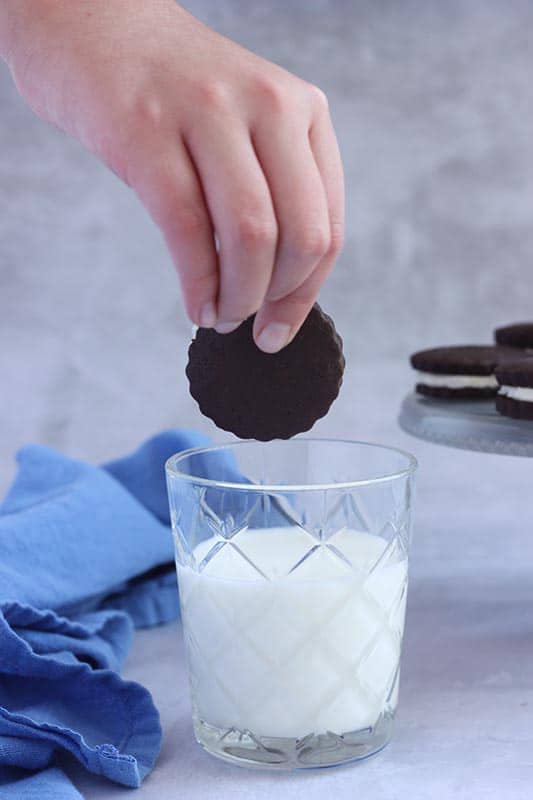 hand dipping chocolate sandwich cookie in milk
